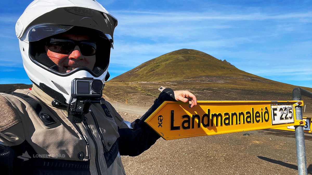 Man wearing a motorcycle helmet posing by an Icelandic road sign.